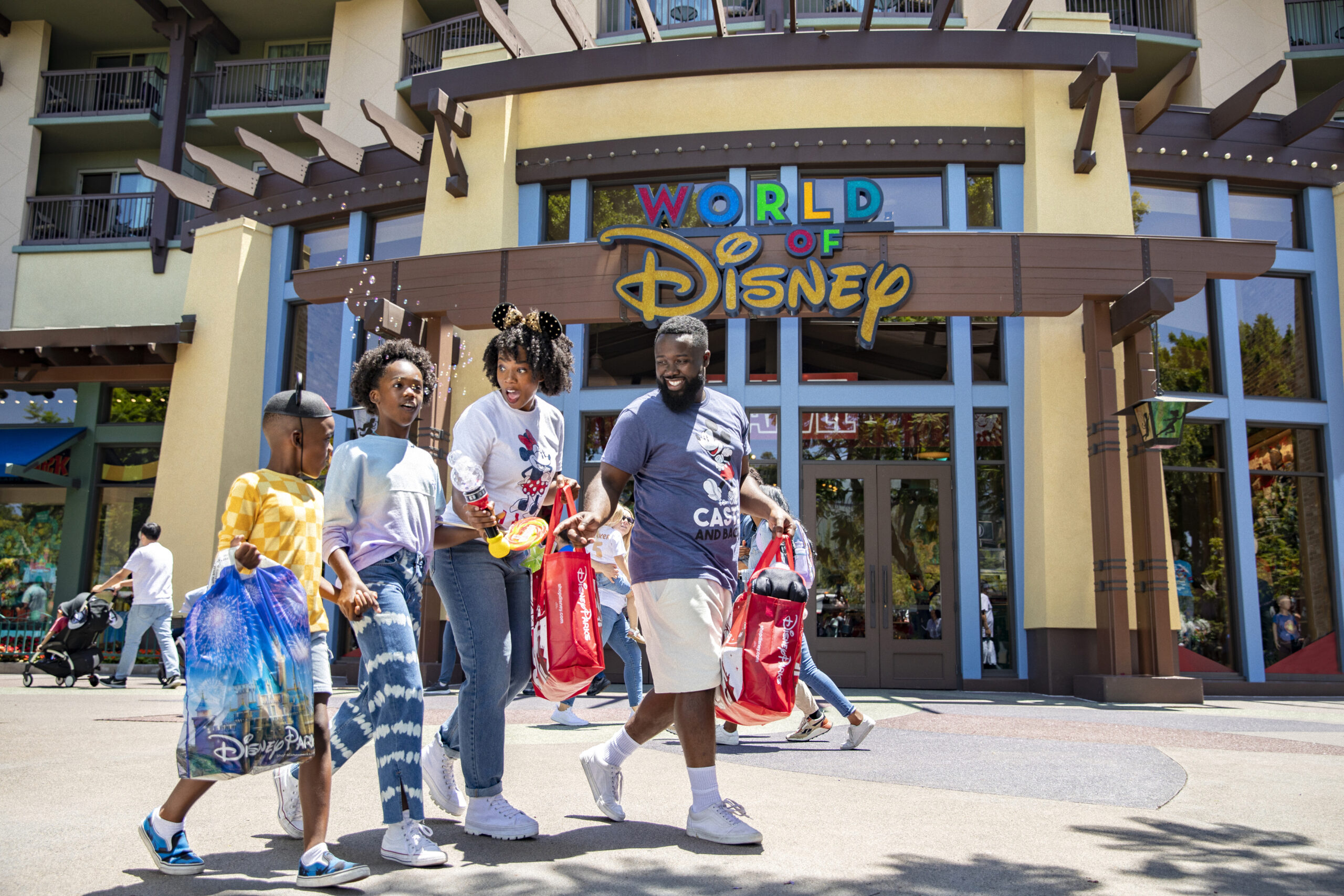 Family happily walking in front of the World of Disney store while holding bags of merchandise
